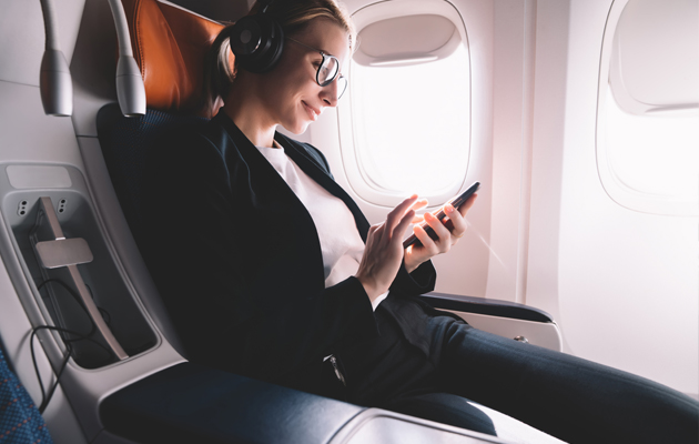Dämpar bakgrundsbuller Kvinna med hörlurar som kollar på sin mobil på ett flygplan.