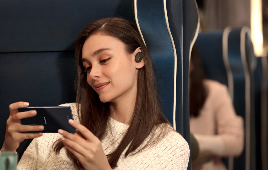 Sony Xperia 5 lyd Kvinnelig togpassasjer som holder en Xperia 5 og har på seg ørepropper