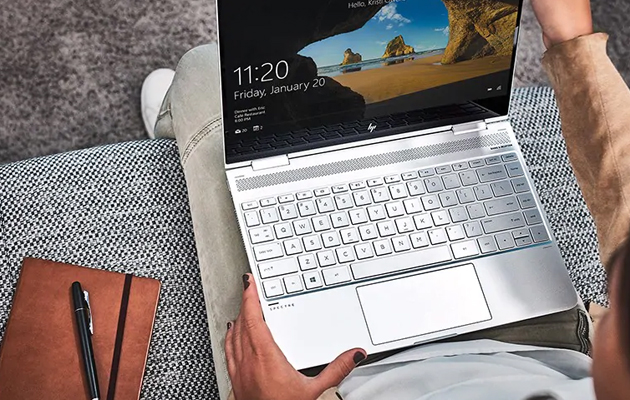Joustava, kuten sinä Nainen istuu sohvalla kannettava sylissään. Kannettavan näytöllä näkyy Windows-aloituskuva.