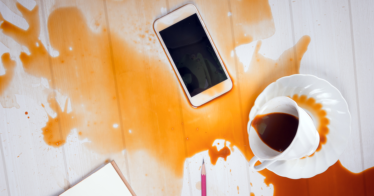 Lær deg hva IP-klassifiseringen betyr En telefon på ett skrivebord med kaffesøl over den