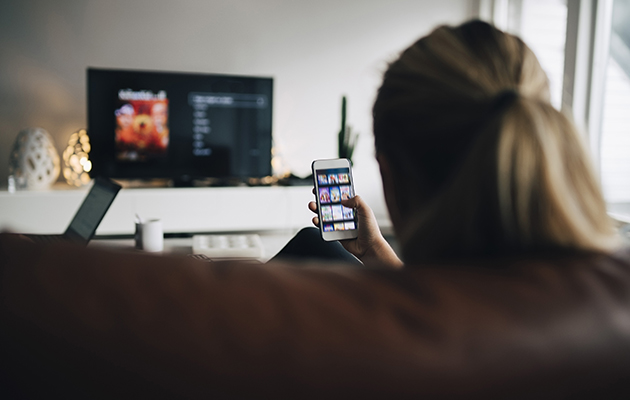 Styr Tven via mobilen En kvinne sitter på en sofa med en mobiltelefon i hånda