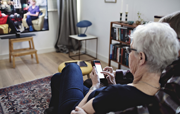 Mange TV-er og smarthøyttalere kan styres med stemmen Bilde av kvinne som styrer TV-en med mobilen