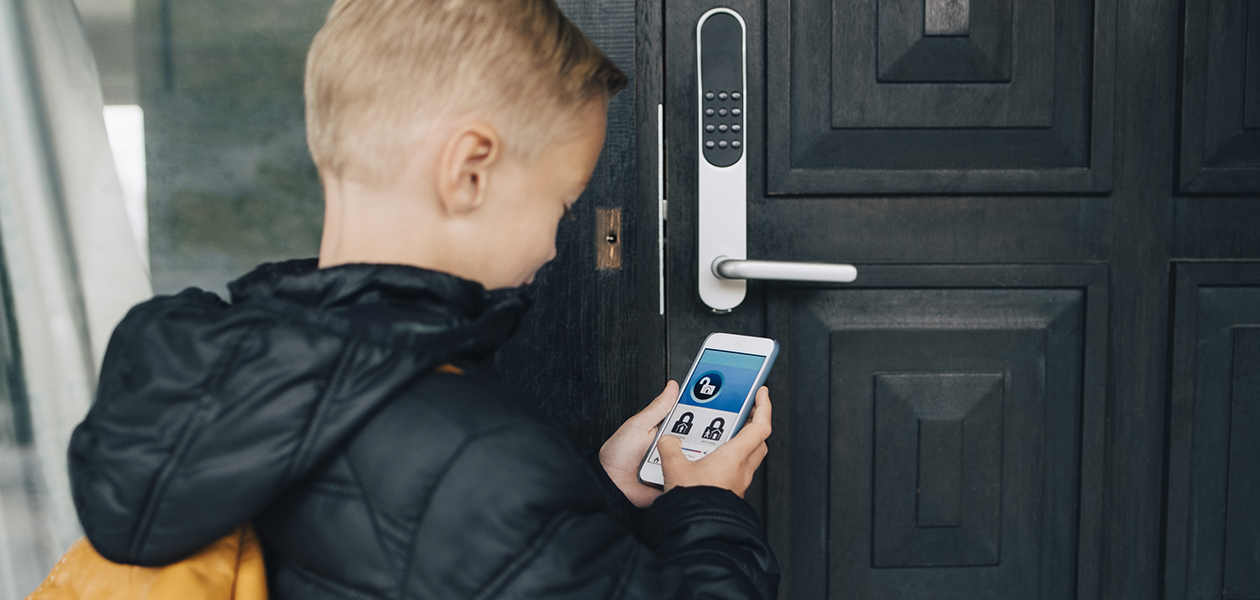 Noen smarte låser kan installeres selv i eldre dører En gutt låser opp en smartlås via en mobilapp.