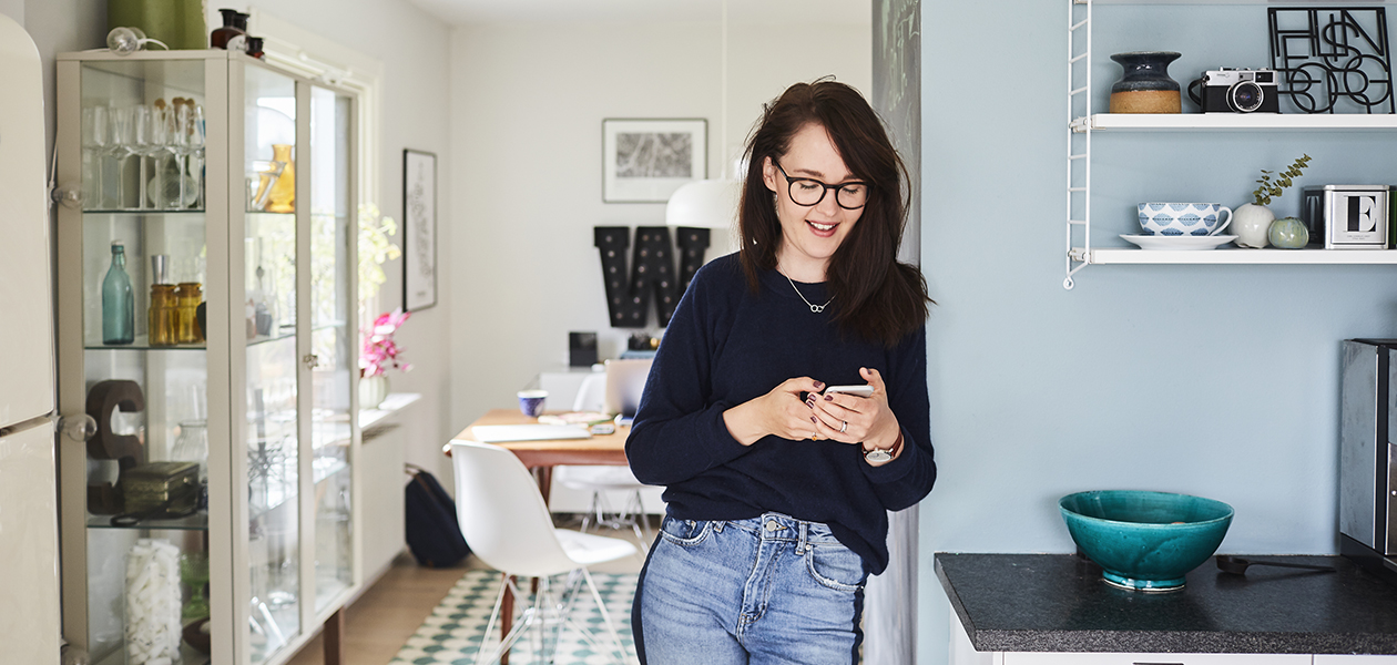 Hvordan ble smarttelefoner så smarte? En kvinne lener seg mot en vegg, holder en smarttelefon i hånda