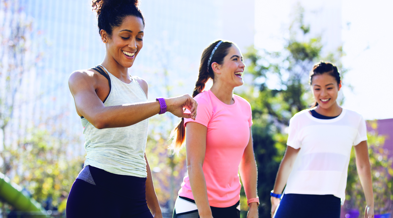 Fitbit aktivitetsmålere Tre kvinner som strekker ut etter trening, alle har Fibit Charge 3 på armen