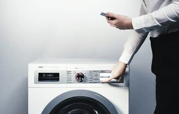 Finn det perfekte vaskeprogrammet i Home Connect-appen En mann holder en mobil og trykker på en knapp på en vaskemaskin.