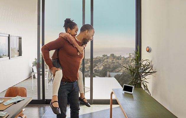 Google Home Hub passer naturlig inn overalt i hjemmet Barn på ryggen til far som begge ser på Google nest hub