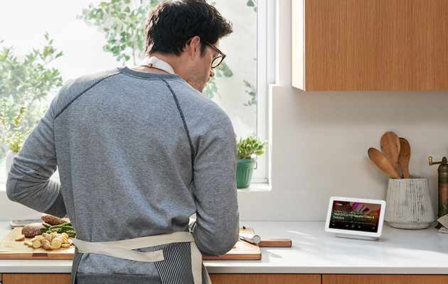 Spill av videoer og sanger fra YouTube Mann som ser YouTube-video på Google Home Hub på kjøkkenet og får hjelp til matlaging