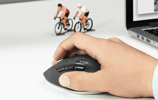 Beveg deg mellom flere skjermer En hånd på en Logitech M720 Triathlon-mus med en bærbar PC og to små sykkelryttere i bakgrunnen