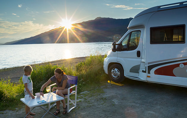 Matlaging på tur kan være utfordrende Bobil parkert ved et vann med solnedgang, en kvinne og et barn sitter ved et campingbord rett utenfor