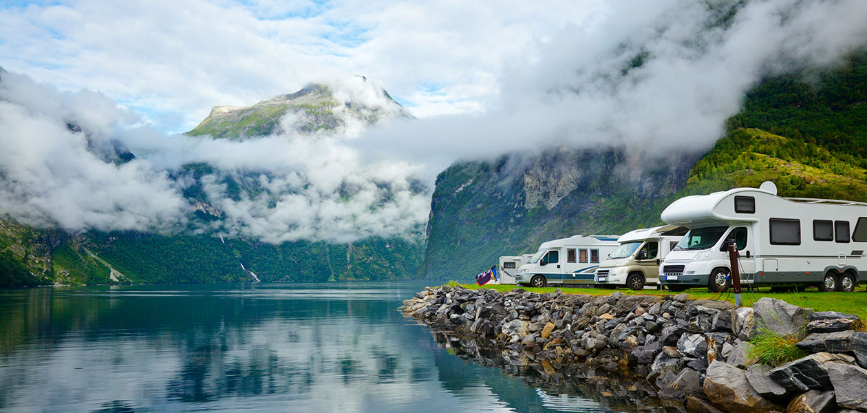 Komfort på camping En rad av hvite bobiler står langs vannkanten, fjell og skyer i bakgrunnen