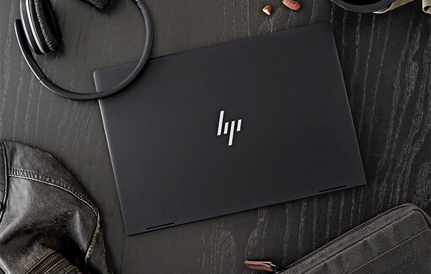 Et design som er både stilig og praktisk HP Envy x360 på et sort bord omgitt av hodetelefoner, en jakke, en veske og nøtter