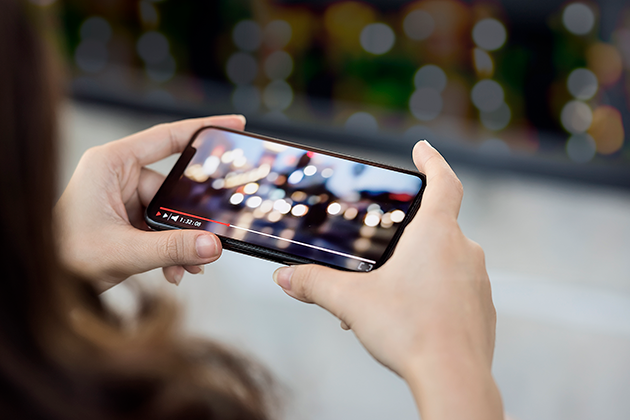 Se film og serier på farten Kvinne som holder mobiltelefon mens hun ser en video
