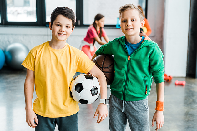Velg riktig sportsklokke til barnet To gutter I en gymsal spiller ball. Den ene gutten har en sportsklokke på.