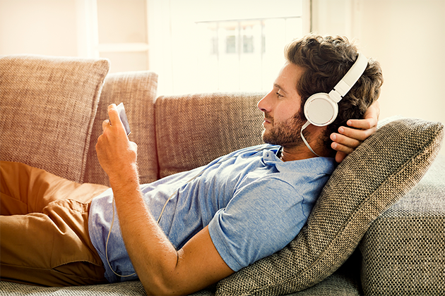 Med en smarttelefon i hånden har du alltid tilgang til underholdning Mann ligger i en sofa og ser på smarttelefonen sin