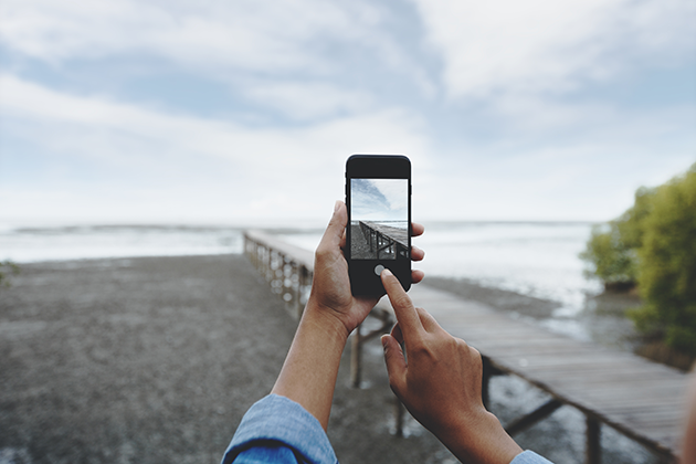 Få tips til hvordan du kan ta bedre bilder med telefonen din Person tar bilde av strand og badebro med mobiltelefonen sin