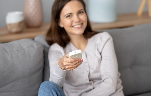 5 tips til hvordan å bruke varmepumpen En smilende kvinne holder en fjernkontroll til en varmepumpe