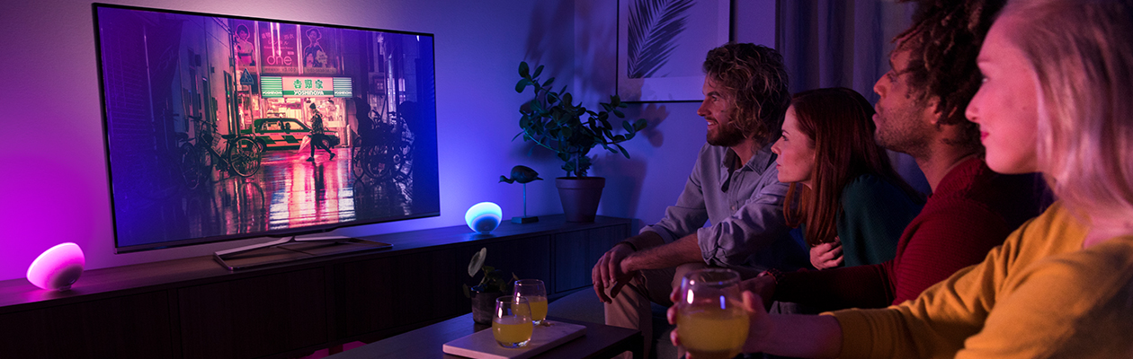 Underholdning To kvinner o gen mann som kicker på TV med Philips Hue-belysning ved siden av