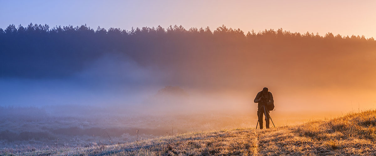 Månedens fotodeal Et tåkete jorde med frost på bakken og silhuetten av en fotograf, lyset er varmt