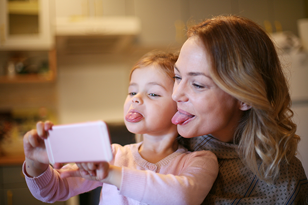 Få plass til flere bilder på mobilen din Kvinne og jente rekker tunge mens de tar bilder med en mobiltelefon
