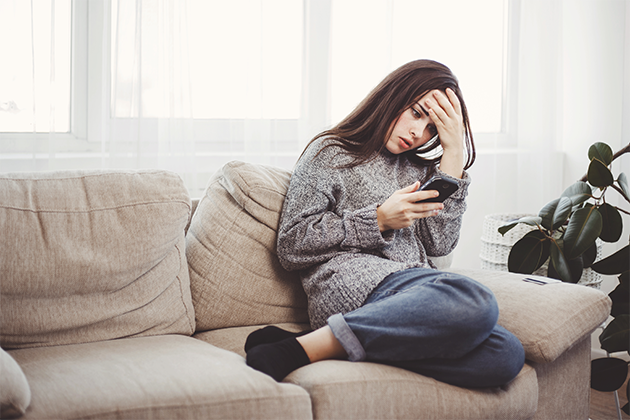 Smarte sikkerhetsregler for å beskytte din telefon Kvinne sitter på en sofa og seg fortvilet på telefonen sin.