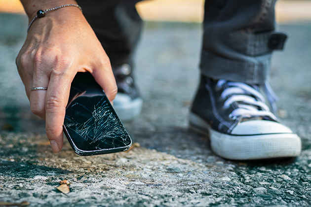 Reparasjon og forsikring Kvinne plukker ødelagt telefon opp fra bakken