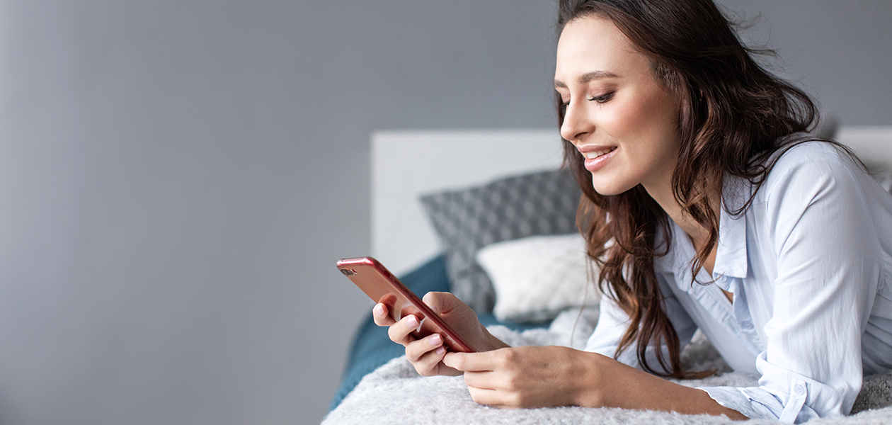 Mindre stress med våre mobiltelefontjenester Kvinne ligger på seng med en telefon