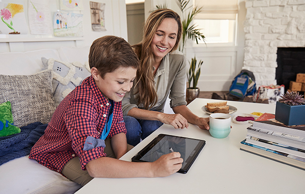 Del Chromebook med hele familien Mor og sønn sitter i en sofa og sønnen tegner på en Chromebook