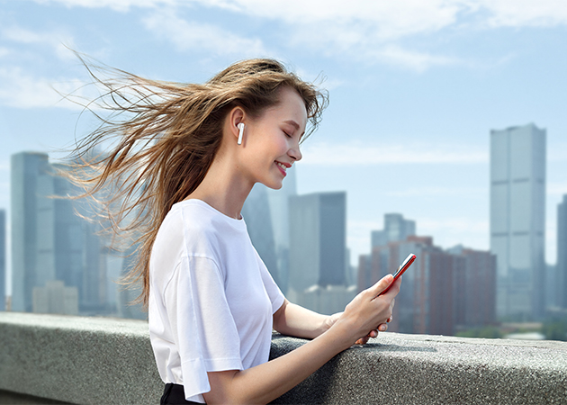 Huawei Freebuds 3 gir deg intelligent støyreduksjon Huawei Freebuds 3 i ørene på en kvinne med skyline i bakgrunnen