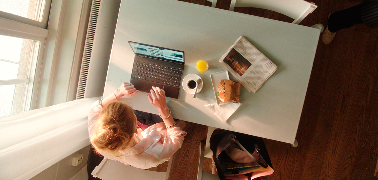 Hvilke funksjoner har den beste bærbare PC-en? Kvinne sitter på kafé med en HP Envy X360