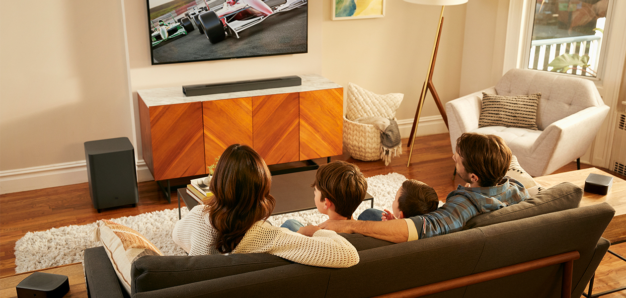 JBL Bar 9.1 lydplanke gir deg helt trådløs 3D-surroundlyd med Dolby Atmos, subwoofer og to trådløse surround-høyttalere JBL Bar 9.1-anlegg i stue med familie som ser TV i sofa