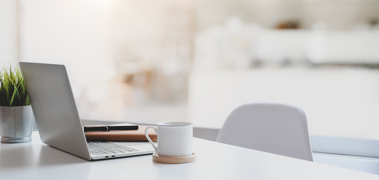 Slik gjør du hjemmekontoret litt bedre Laptop, kaffekopp og notatbok på et hvitt bord