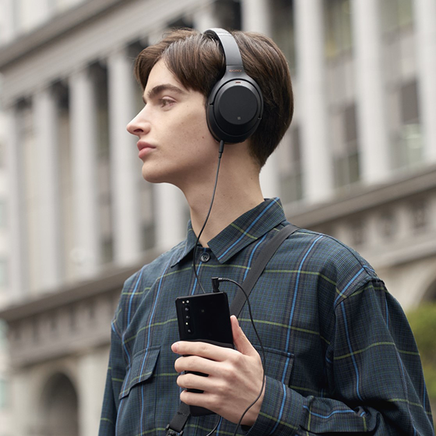 Den ultimate lydkvalitet – med kabel eller trådløst. Mann med Sony hodetelefoner på og Sony Xperia 1 II I hånden