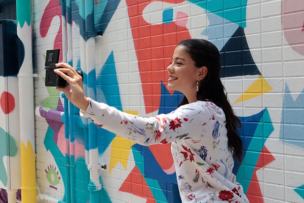 Canon EOS M200 Kvinne tar selfie med et EOS M200 foran en fargerik vegg