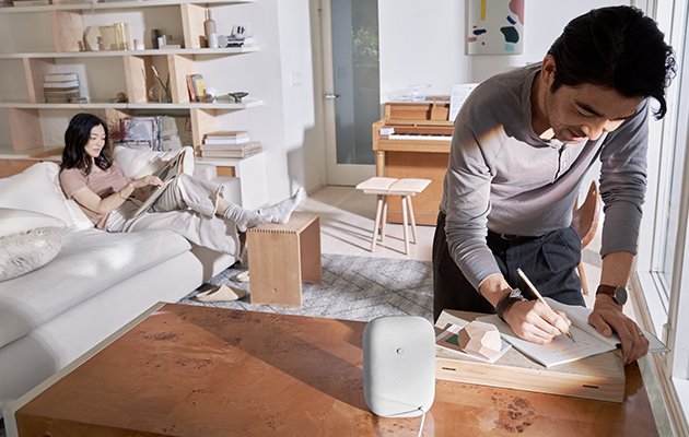 Nest Audio fungerer sammen med hundrevis av kompatible smartenheter Google Nest Audio på bord foran mann og kvinne i bakgrunnen