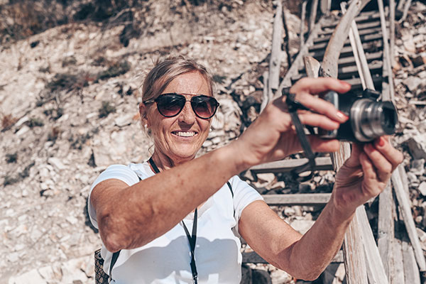 Smilende, eldre kvinne på strand med kompaktkamera i hendene