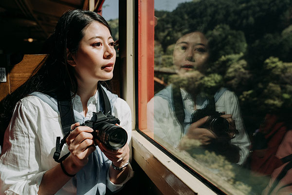 Asiatisk kvinne med systemkamera i hendene sitter og ser ut av vinduet på et tog