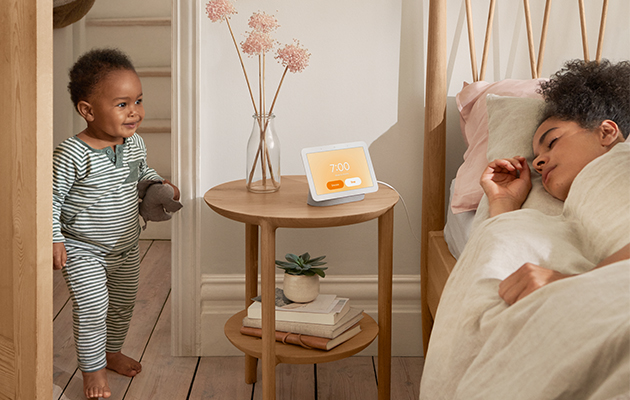 Med Nest Hub på nattbordet blir det lettere å sovne og våkne Gutt kommer inn på rom hvor kvinne sover med Google Nest Hub på nattbord