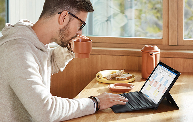En Windows 10 for alle Mann som drikker kaffe foran et nettbrett med tastatur