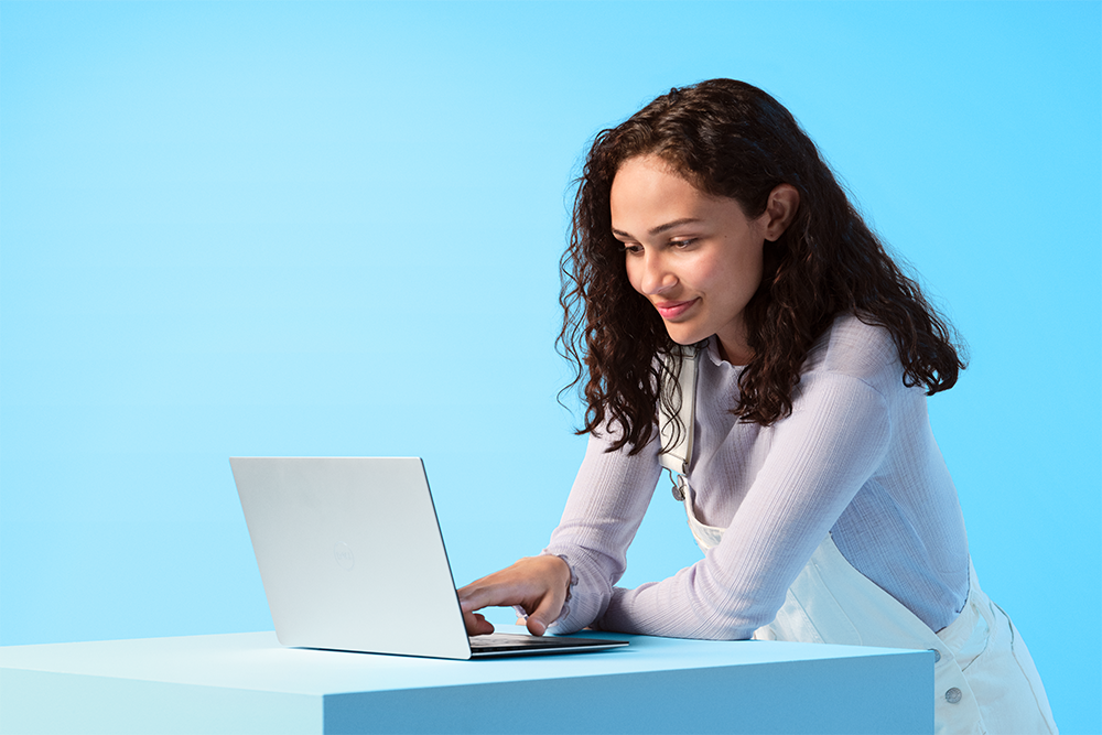 Windows 11 lar deg maksimere produktiviteten Kvinne som sitter med en Windows 11 PC foran seg på et blått bord