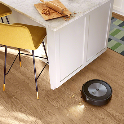 Roomba® j7/Roomba® j7+ -robotstøvsuger En svart robotstøvsuger som støvsuger et kjøkkengulv