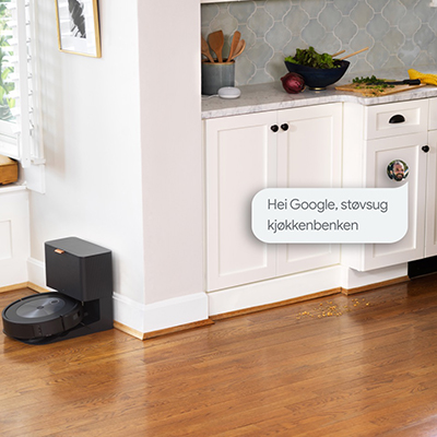 Roomba® j7/Roomba® j7+ -robotstøvsuger En robotstøvsuger parkert på ladestasjon og et kjøkken med en snakkeboble