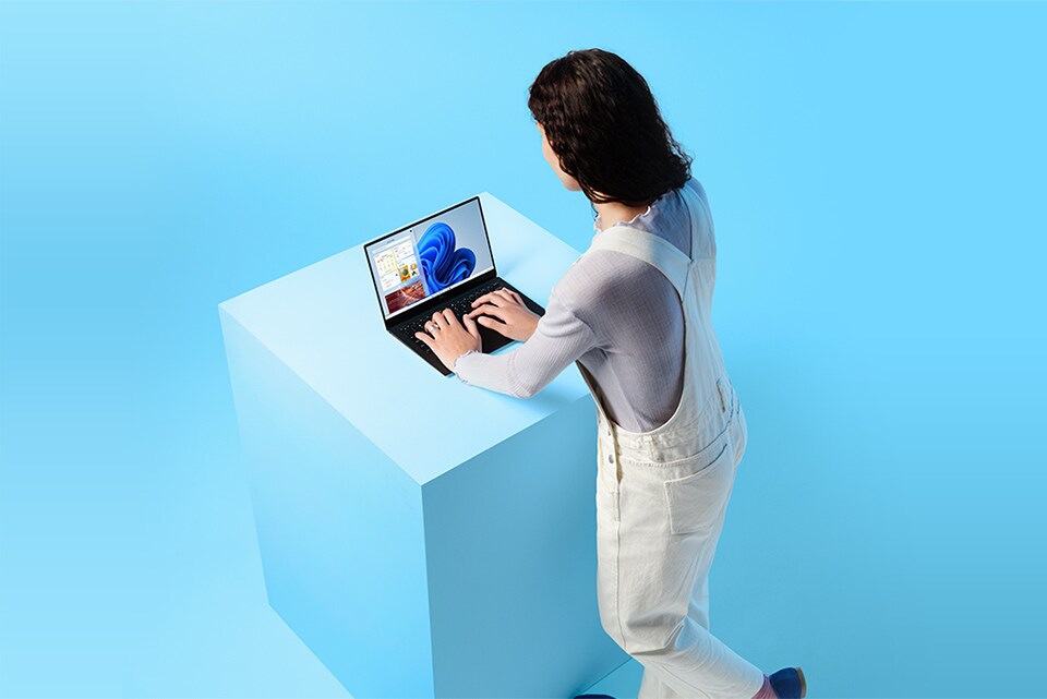 Kvinne står med Windows 11-laptop på en blå kube