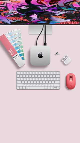Mac mini vist ovenfra, aluminium i sølv, avrundede hjørner, blank svart Apple-logo i midten, koblet til med kabel, Studio Display er delvis synlig ovenpå. AirPods 4 er åpne, og det vises fargeprøver i Pantone samt et Logitech-tastatur og en Logitech-mus i rødt.