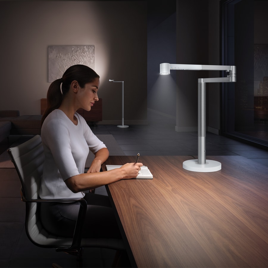 Kvinne sitter ved et bord med en Dyson lampe foran seg
