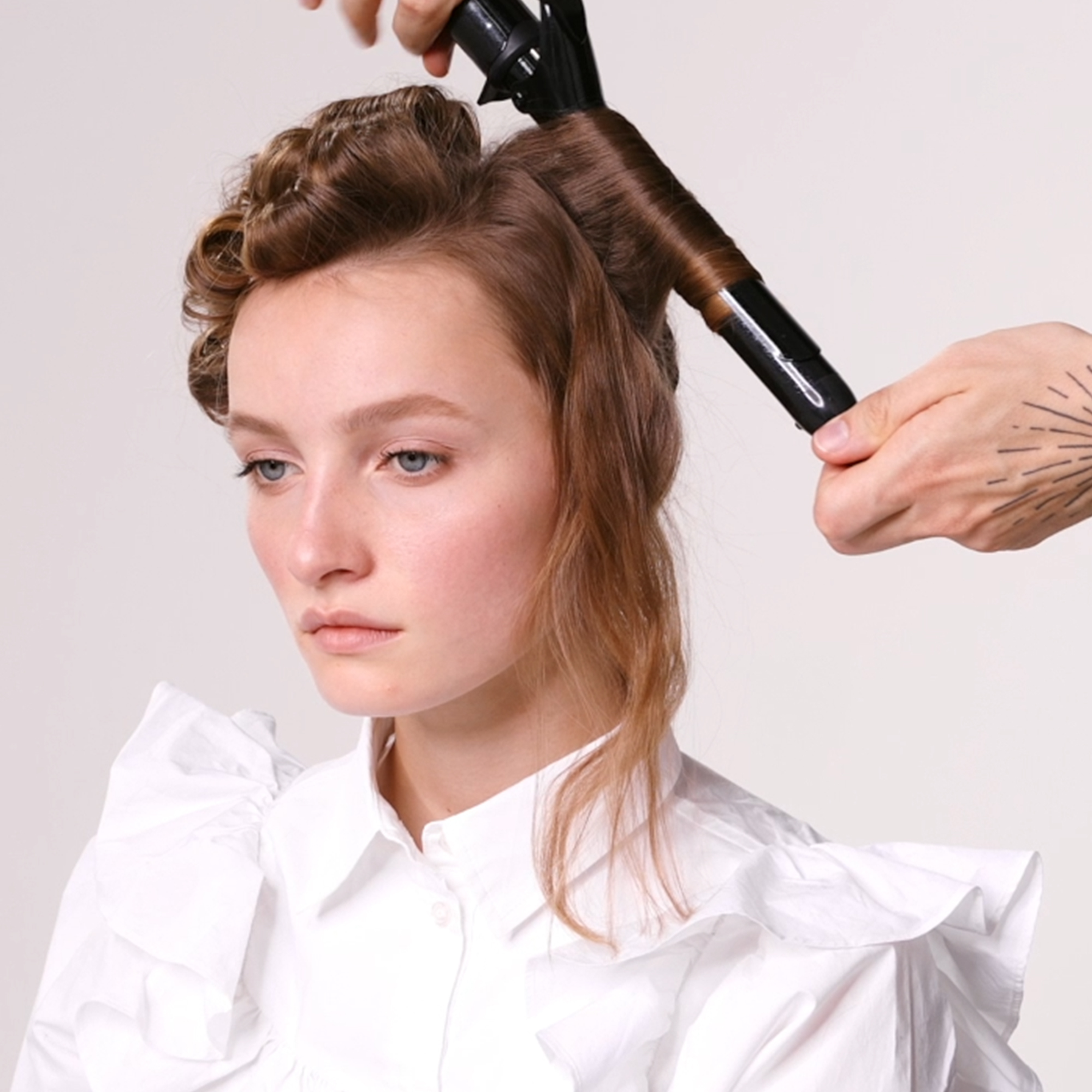 Kvinne med brunt hår og en hender med en BaByliss Pro krølltang som krøller den bakre delen av håret hennes