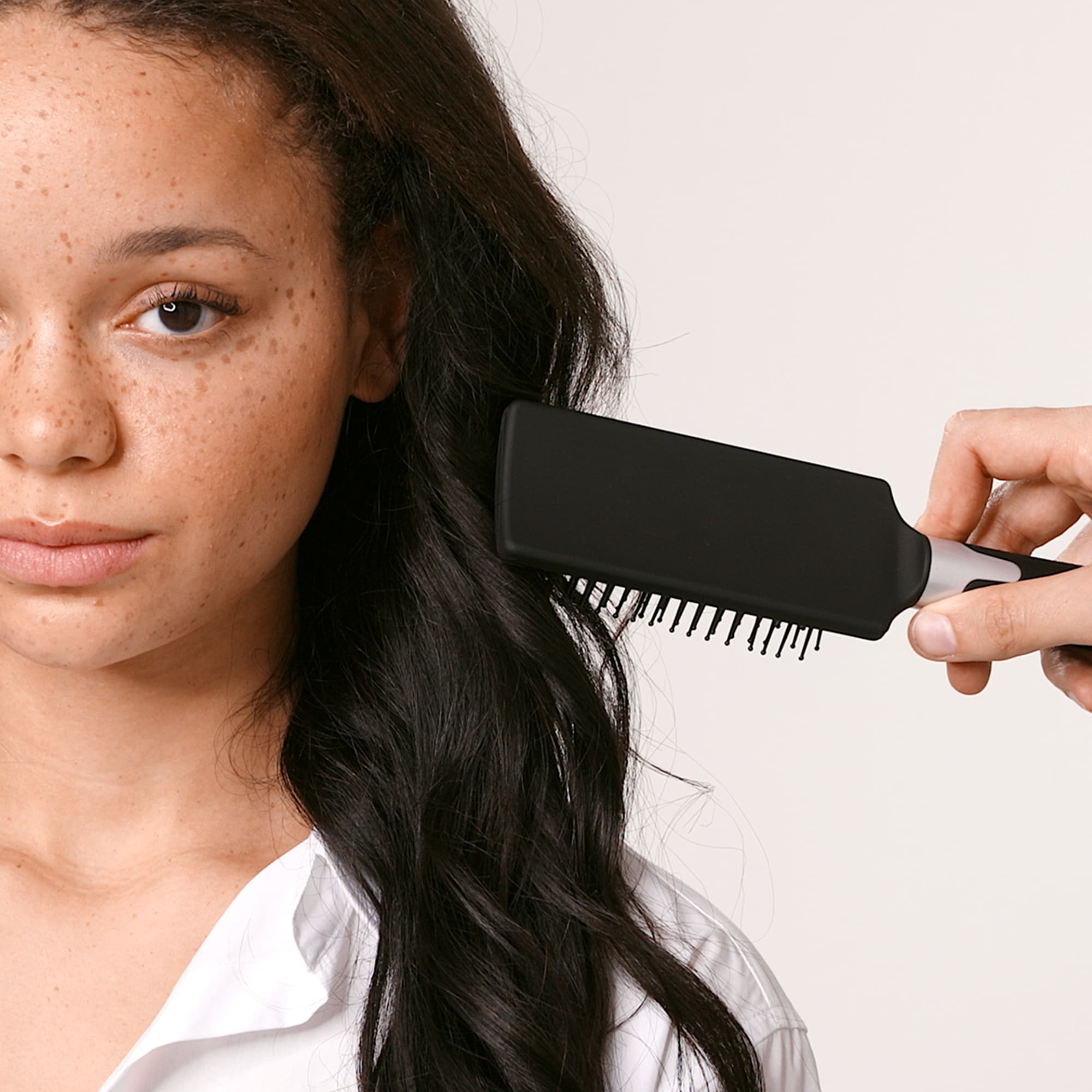 Kvinne med mørke krøller og en hårbørste som grer gjennom håret 