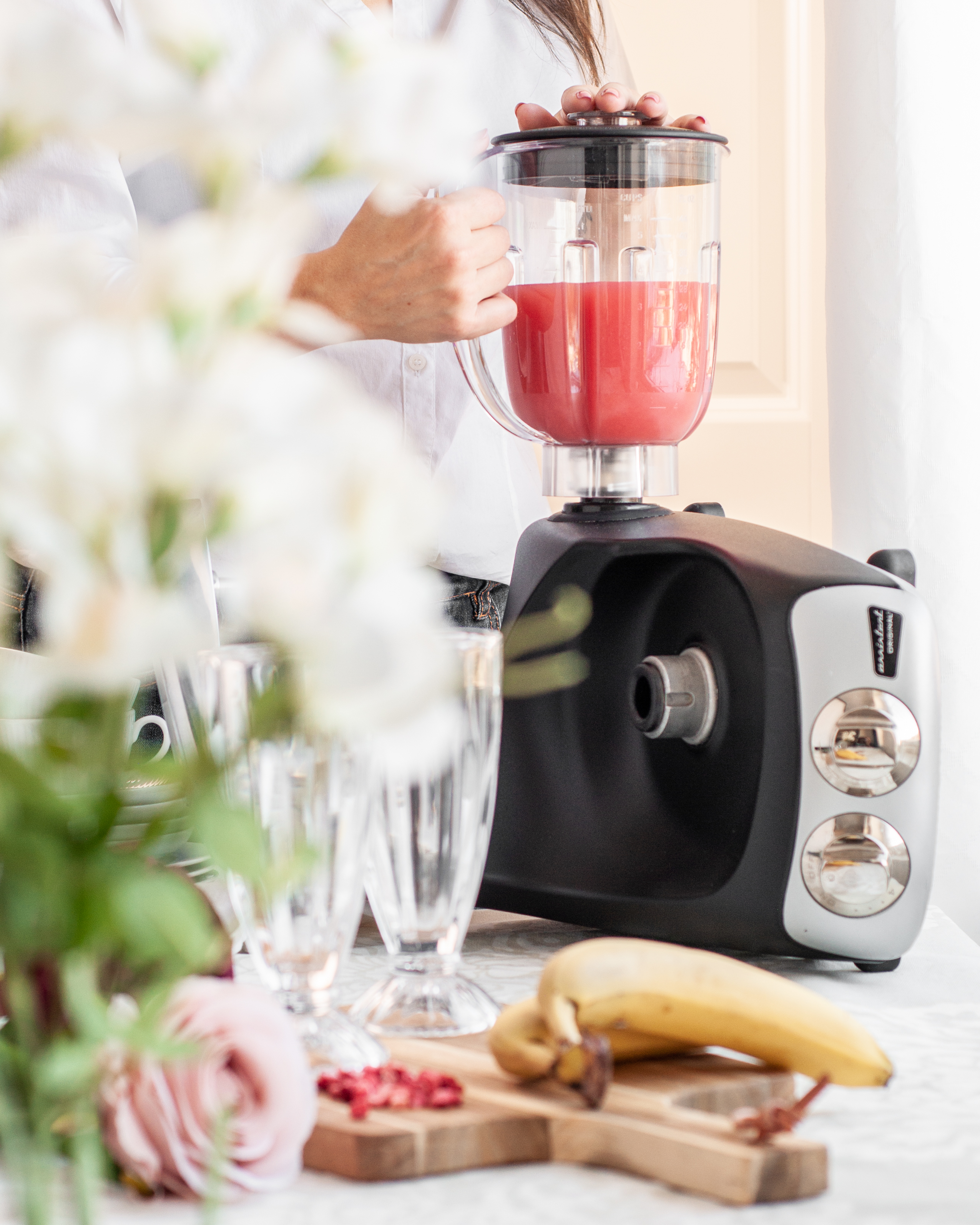 En kvinne holder en Ankarsum Assistant blender som inneholder rosa juice på en kjøkkenbenk