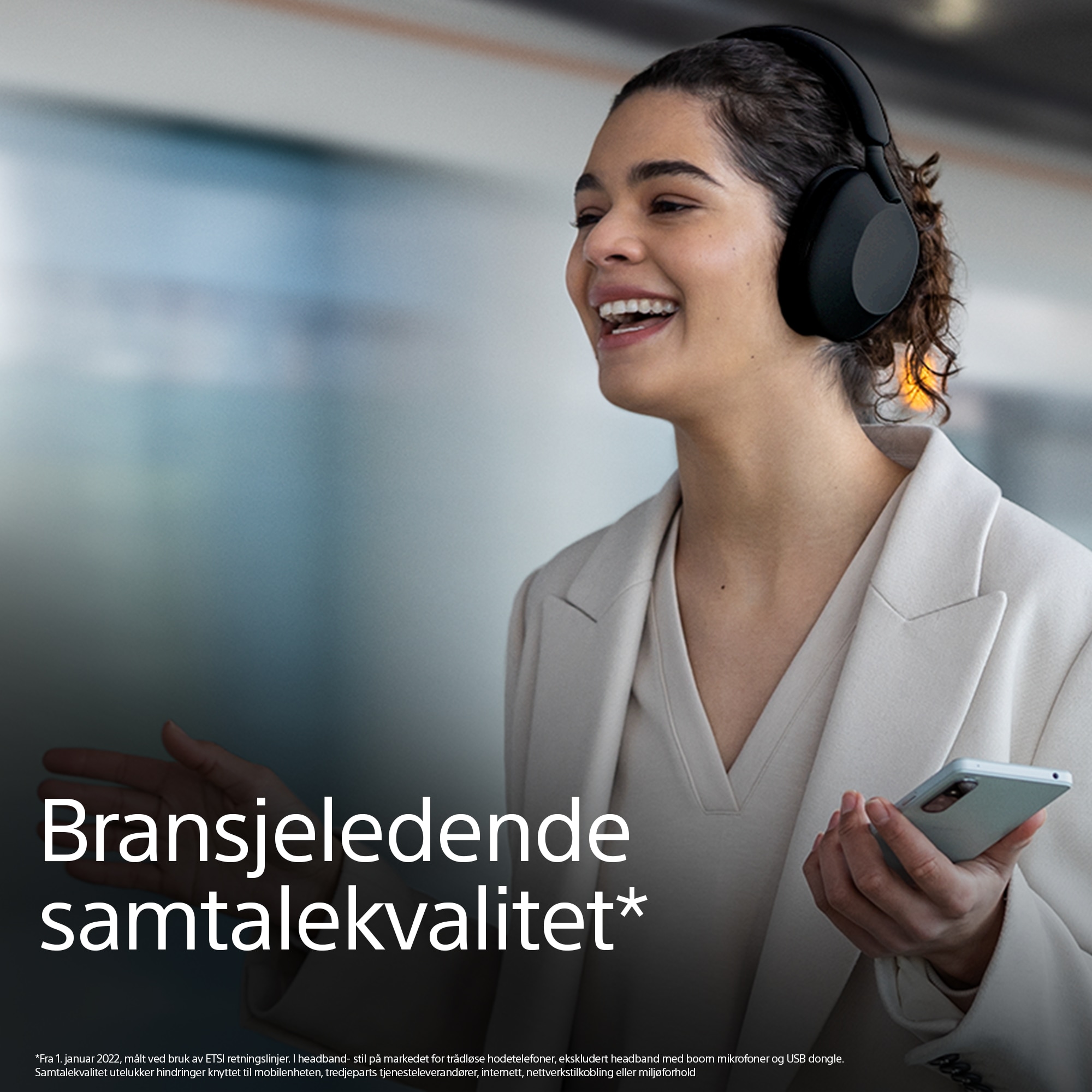 En smilende kvinne har på seg Sonys WH1000XM5 og teksten bransjeledende samtalekvalitet