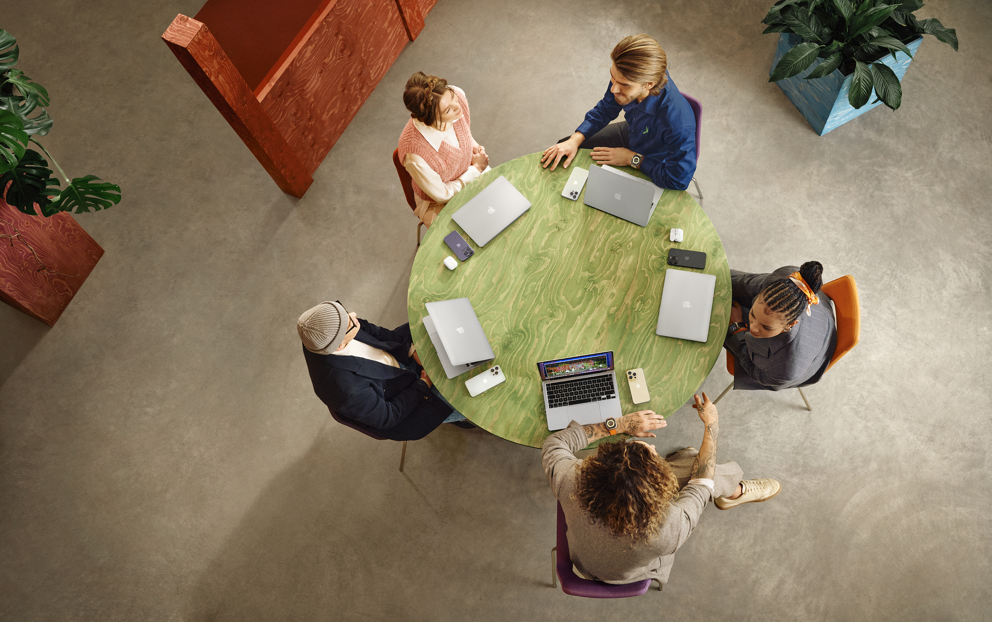 Team snakker rundt et bord med Apple-produkter